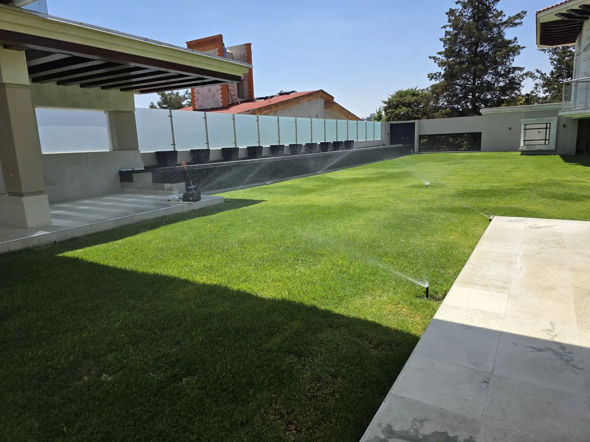 Jardín de pasto de una casa moderna con aspersores regando junto a la terraza