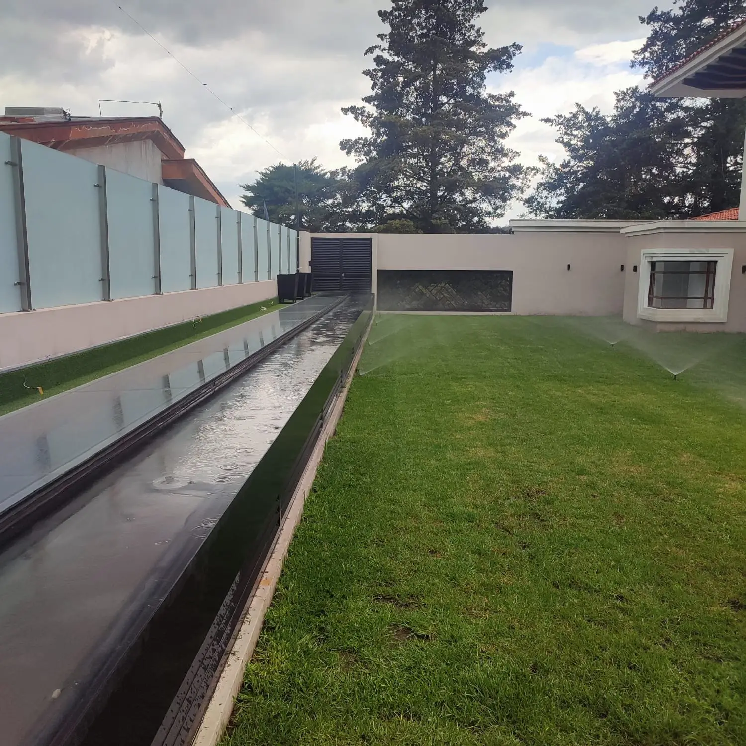 Pasto alargado junto a un espejo de agua con aspersores funcionando