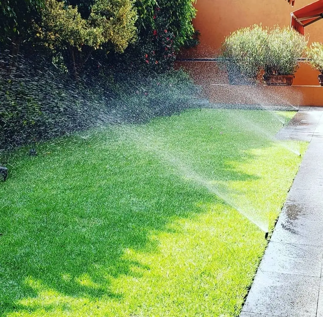 Jardín con pasto y deck de madera regado por aspersión